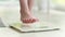 Female legs stepping on white scale at home. Bare feet on a weight scale.
