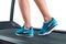 Female legs in turquoise sneakers on a treadmill.
