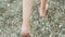 Female legs walking on pebbles beach at summer vacation. Close up barefoot girl feet stepping on pebbles at summer sea
