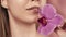 Female lips with delicate pink lipstick and orchid flower closeup on a pink blurred background. A beautiful white smile