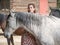 Female looking at camera with grey horse in front.