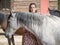 Female looking at one side with grey horse in front.