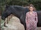 Female looking to camera while leaning on a black horse