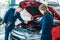 Female and male Sales managers of a car showroom looking under car