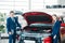 Female and male Sales managers of a car showroom standing near car with open