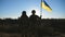Female and male soldier of ukrainian army standing at peak of hill with raised flag of Ukraine. Military couple in