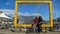 Female and Male tourist with face masks on sitting on big yellow frame which frames Table Mountain.