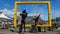 Female and male Tourists with face mask sitting on big yellow frame which frames table mountain. The man is a paraplegic and is