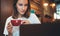 Female manager holding in hands cup of coffee looking screen laptop in cafe, girl freelancer relaxing with cappuccino