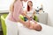 Female massage therapist or a doctor examining newborn baby boy with the mother watching in the background. Baby massage concept.