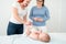 Female massage therapist teaching young mother how to massage her newborn baby boy. Baby massage concept.