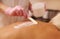 Female masseur applies a massage cream scrub using a wooden spatula to the back of a young woman lying on a massage table and