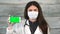 Female medic in white coat and protective mask holding in hand smartphone
