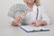 Female medicine worker in cabinet smiling and holding money isolated.