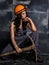 female miner worker with pickaxe, in coveralls over his naked body, sitting on the floor on backdrop of steel wall