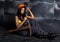 female miner worker with pickaxe, in coveralls over his naked body, sitting on the floor on backdrop of steel wall