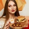 Female model demonstrating burger lying on round wooden plate