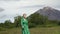 Female model dressed in green leather coat walking in forest on backdrop of volcano on summer day