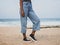 Female modeling vintage light blue denim pants with black and white shoes at the beach