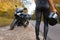 Female motorcyclist in leather clothes stands on the side of the road holding helmet in hand.