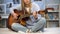 Female musician tuning the guitar on home sofa, enjoying melody, practicing