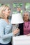 Female Neighbor Helping Senior Woman Change Lightbulb In Lamp