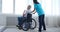 Female nurse taking care of disabled elderly man on wheelchair looking out through window