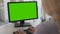 Female office worker typing documents on personal computer with green screen