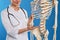 Female orthopedist with human skeleton model on background, closeup