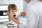 Female paediatrician examining little kid patient throat with wooden stick