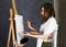 Female paint artist posing next to a easel and paints on an canvas, depicts a reverie