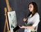 Female paint artist posing next to a easel and paints on an canvas, depicts a reverie