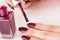 Female with paint brush and bottle applying red wine manicure nails polish on finger
