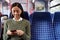 Female Passenger Sitting In Train Looking At Mobile Phone