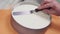 Female pastry cook using icing spatula on creme in baking form on turntable