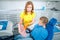 Female pediatric dentist medic making a treatment for adorable little smiling girl sitting in chair in a hospital