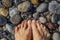 Female pedicured tanned feet on rocky sea beach, visible through clear water.