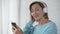 Female pensioner in headphones listening to song on mobile phone and dancing