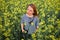 Female photographer wearing a shirt with stripes scouts around in the middle of a rapeseed field