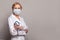 Female physician wearing in uniform and protective medical mask on grey background