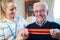 Female Physiotherapist Helping Senior Man To Use Resistance Band At Home