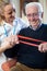 Female Physiotherapist Helping Senior Man To Use Resistance Band At Home