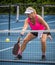 Female pickleball player digs out a low shot to dink the ball over the net