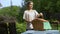 Female placing wicker picnic basket on table, outdoor picnic in country house