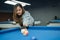 female pool player with solemn face poking the white ball