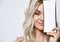 Female posing  on white. Smiling, covering half of her face by packaging of beauty product with copy space. Close up