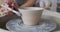 Female potter paints rotating pot on the pottery wheel.