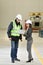 Female project manager in a business suit and white hard hat holds laptop and discusses product details with the chief engineer