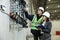 Female project manager in a business suit and white hard hat holds notebook and discusses product details with the chief engineer