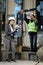 Female project manager in a business suit and white hard hat holds notebook and discusses product details with the chief engineer